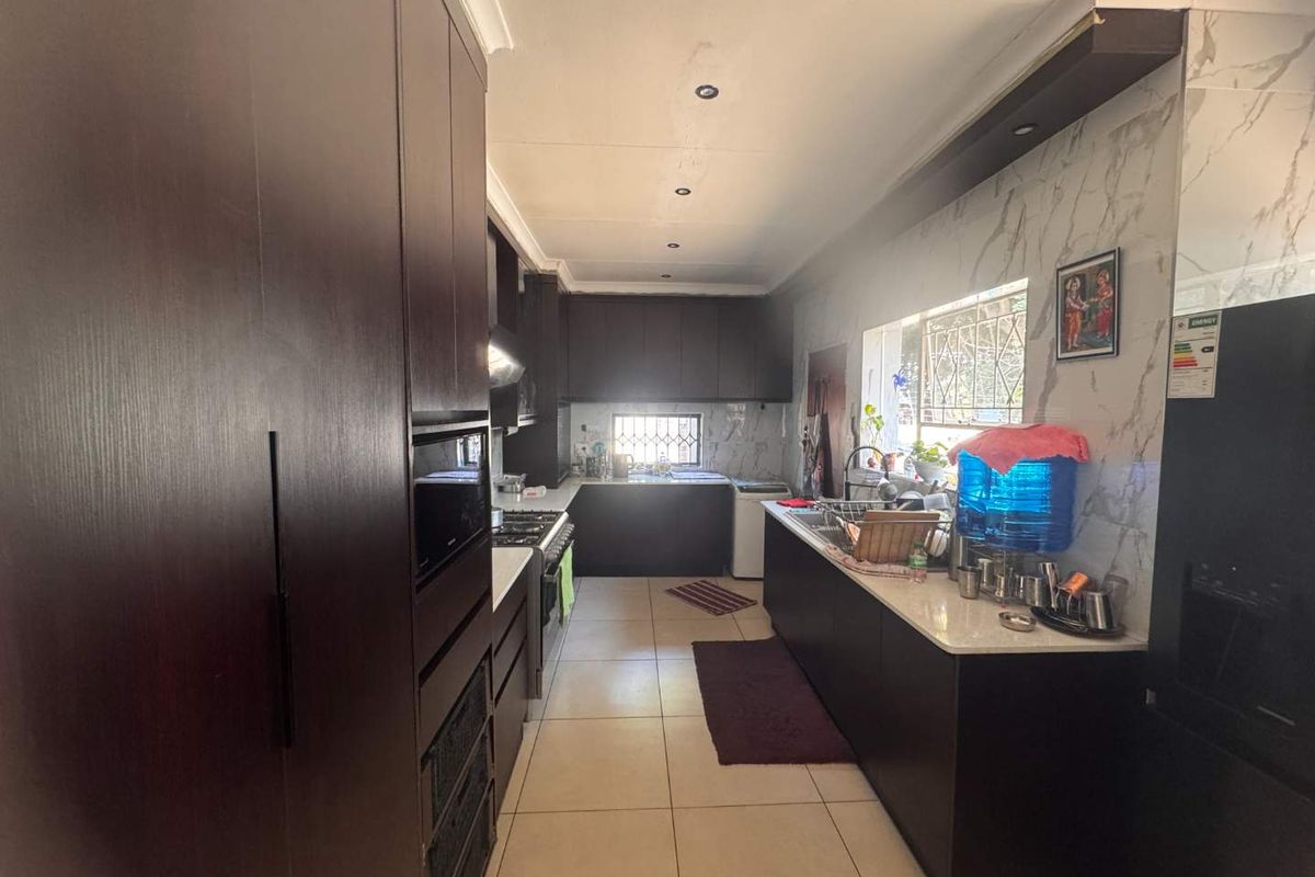 A functional galley-style kitchen featuring dark wood cabinetry, stone countertops, marble-look splashbacks, and integrated appliances with tiled flooring throughout.
