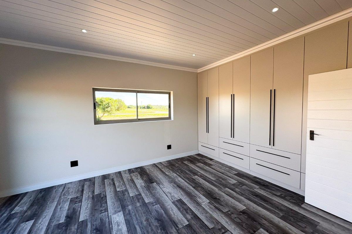 A bright, modern bedroom featuring extensive built-in cabinetry, wood-look laminate flooring, and a tongue and groove ceiling with recessed lighting.