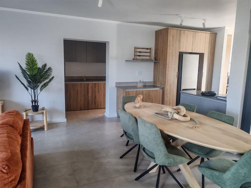 Modern open-plan living and dining area featuring contemporary wood-finish cabinetry, stone countertops, and sleek tiled flooring with seamless access to the adjacent scullery.