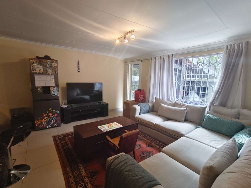 A comfortable living room featuring tiled flooring, ceiling cornice detailing, and a security gate over the window, providing a functional and secure living space.