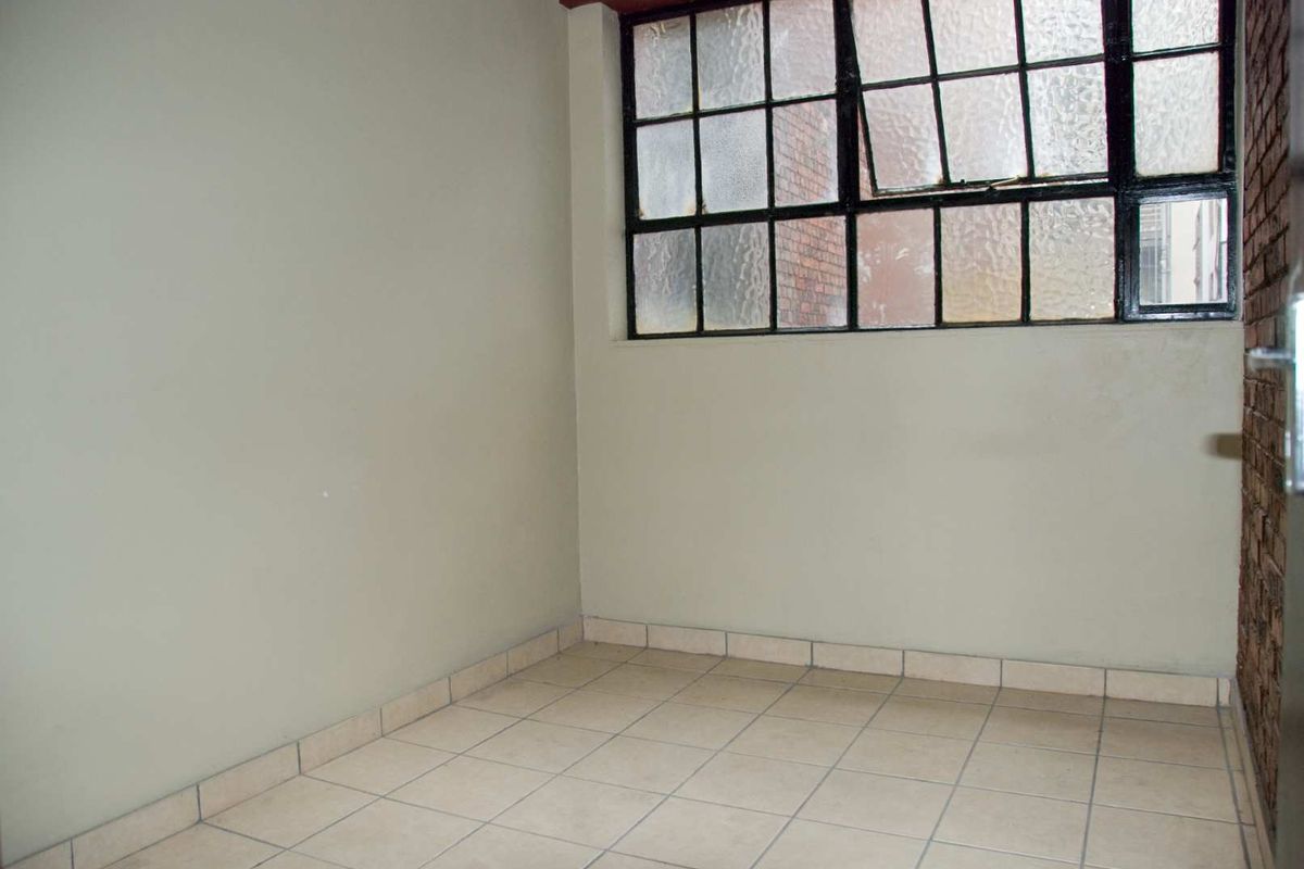 An empty bedroom featuring industrial-style steel frame windows, tiled flooring, and an exposed brick wall accent.