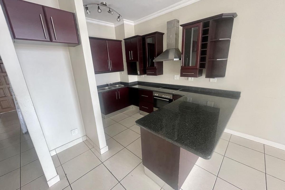 A functional kitchen featuring dark wood cabinetry, granite countertops, a breakfast bar, and built-in appliances including an oven, hob, and extractor fan.