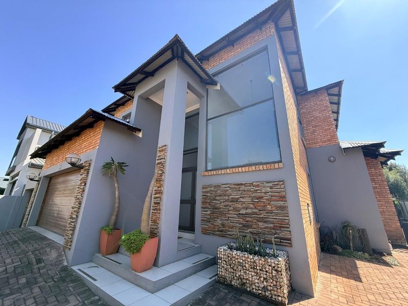 Modern double-storey home featuring a striking combination of brick and grey plaster finishes, stone cladding accents, and a paved driveway.