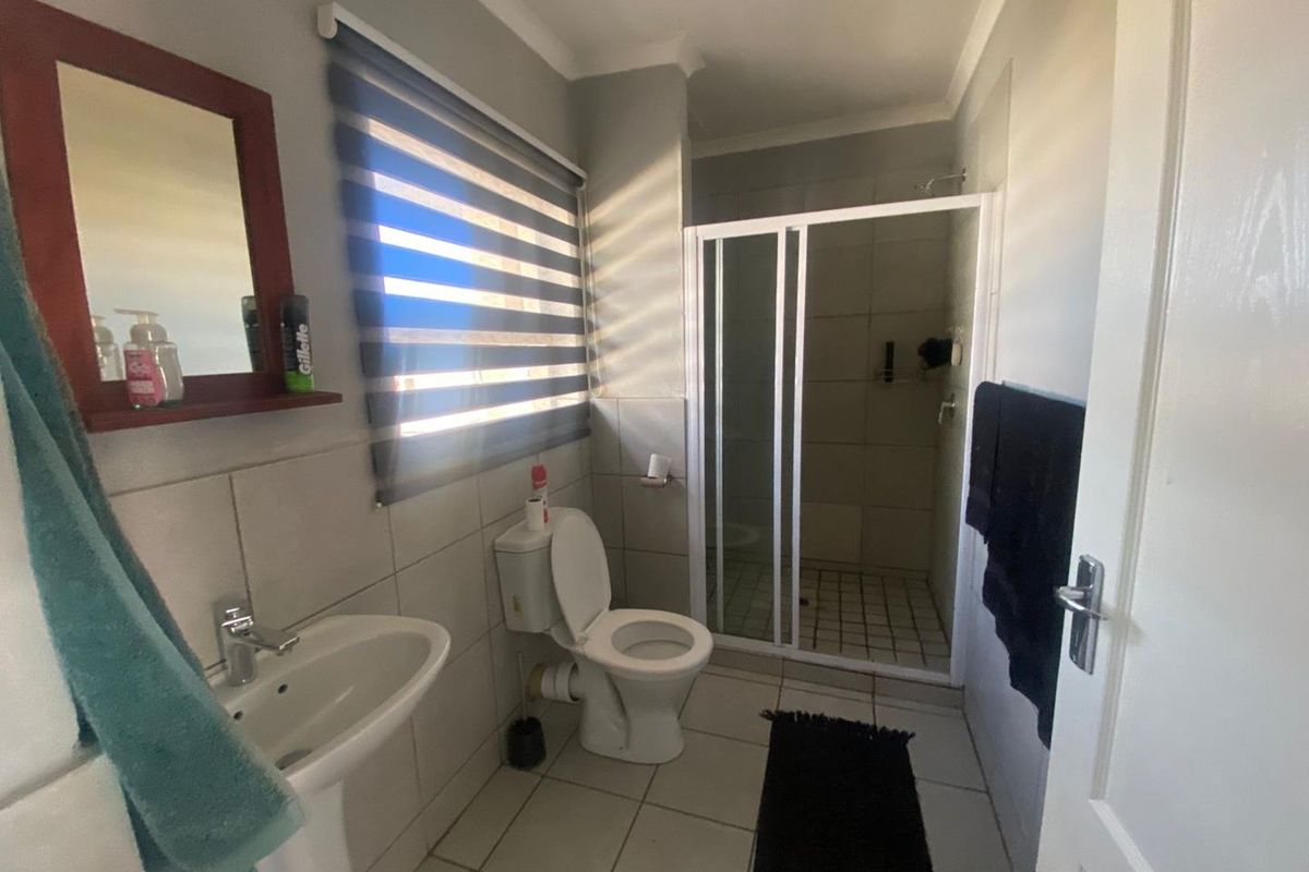 A functional bathroom featuring a pedestal basin, a standard toilet, and a glass-enclosed shower with tiled flooring and walls.