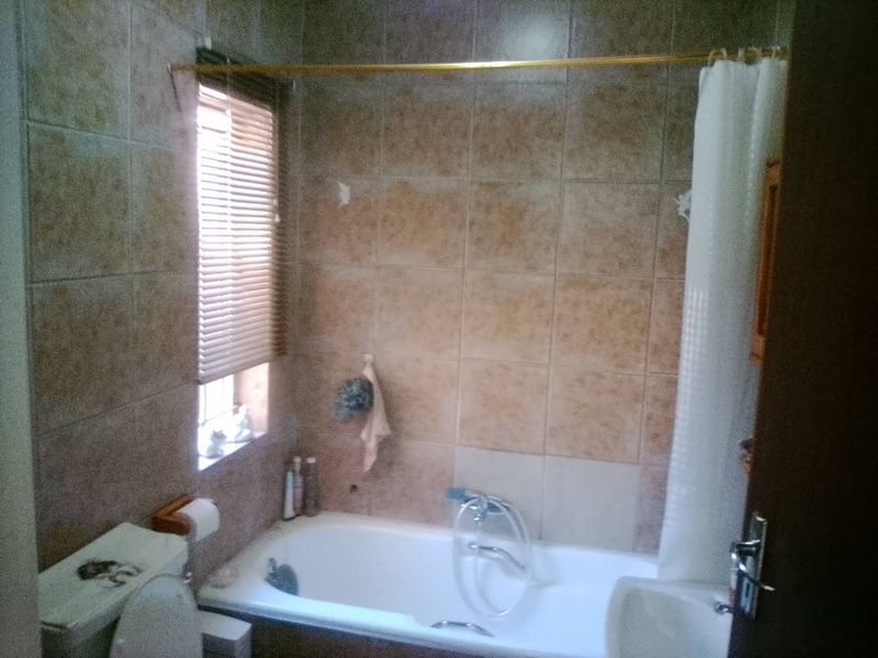 A dated bathroom featuring a bathtub with shower mixer, toilet, and tiled walls. The space requires cosmetic updates to improve its overall condition.