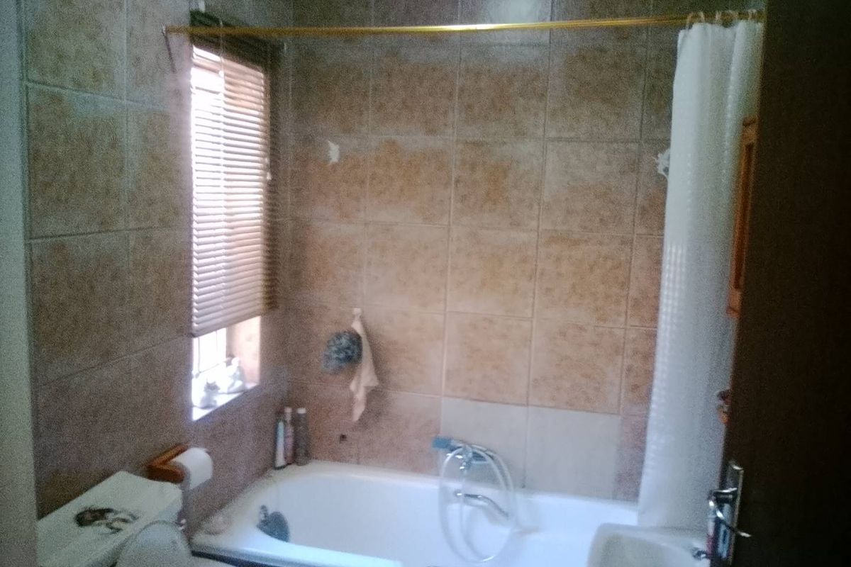 A dated bathroom featuring a bathtub with shower mixer, toilet, and tiled walls. The space requires cosmetic updates to improve its overall condition.