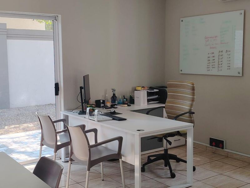 A functional home office space featuring tiled flooring, a wall-mounted whiteboard, and direct access to an outdoor area through a sliding glass door.