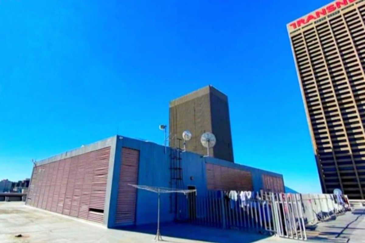A rooftop terrace area featuring concrete flooring, metal security fencing, and utility structures, offering an open outdoor space with urban views.
