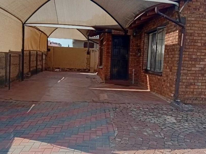 Front exterior view featuring a paved driveway, brick facade, and a large shade sail carport structure.