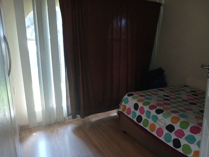 A functional bedroom featuring laminate flooring, a built-in cupboard, and a sliding door providing access to the exterior.