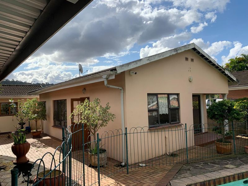 Rear view of the cottage featuring a paved patio area, metal perimeter fencing, and exterior wall finishes with visible maintenance requirements on the eaves.