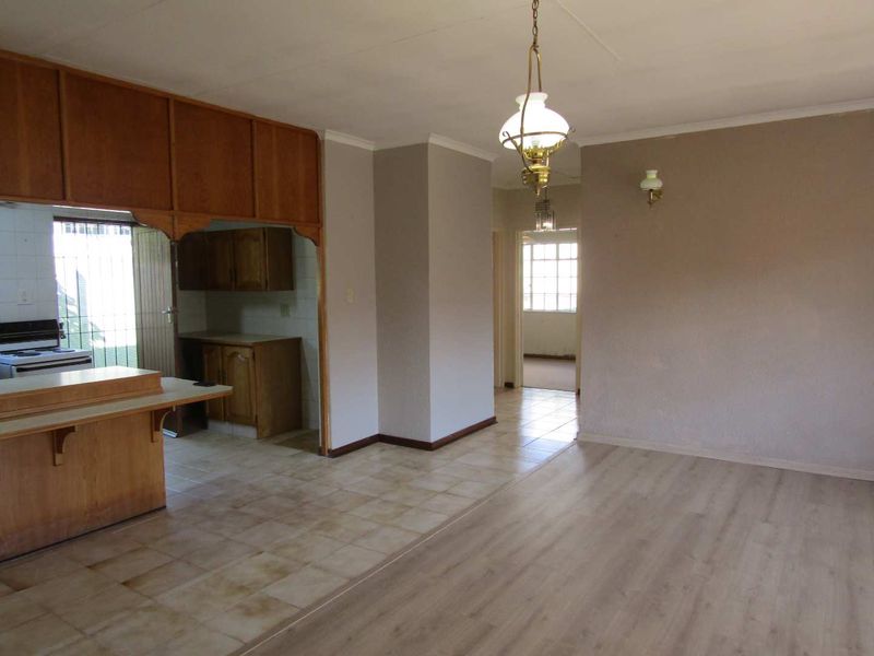 Open plan living and kitchen area featuring a mix of laminate and tiled flooring, dated wooden cabinetry, and traditional pendant lighting.