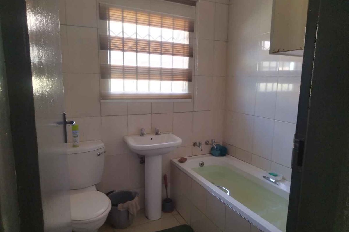 A functional bathroom featuring a pedestal sink, standard toilet, and a built-in bathtub with tiled walls and a window.