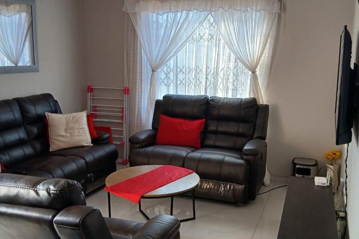 A comfortable living room featuring tiled flooring and a window fitted with security bars, providing a functional and well-lit space.