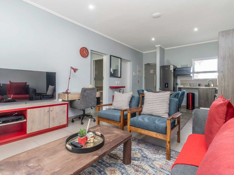 An open-plan living and kitchen area featuring tiled flooring, recessed lighting, and functional kitchen cabinetry with a built-in counter and sink.