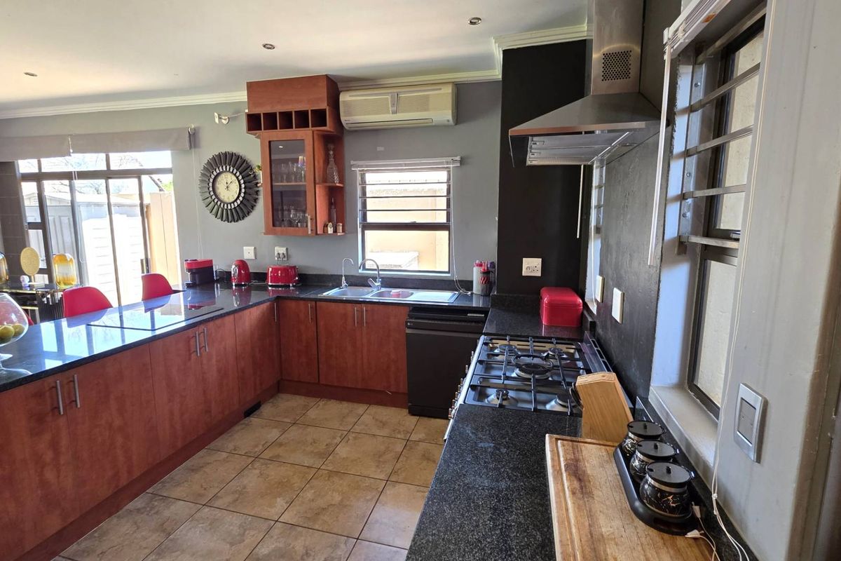 A functional kitchen featuring dark granite countertops, wood-finish cabinetry, a gas hob with extractor fan, and tiled flooring.