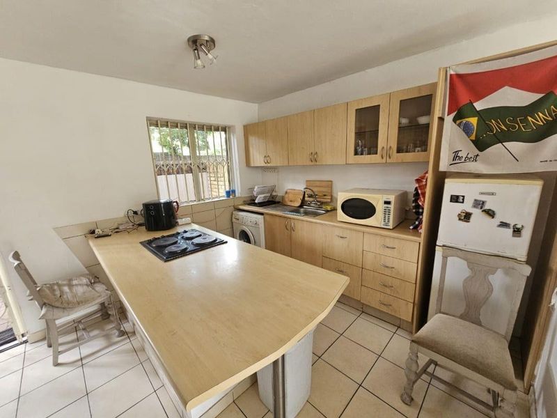 Functional kitchen featuring light wood cabinetry, laminate countertops with an integrated hob, tiled flooring, and a window with security bars.