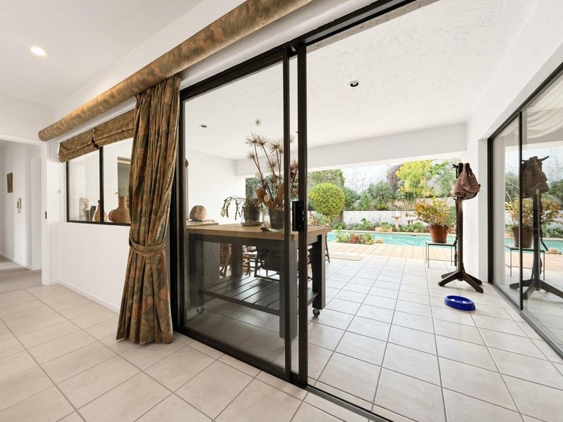 Covered patio area featuring tiled flooring and large sliding glass doors, providing seamless access to the outdoor swimming pool and garden space.