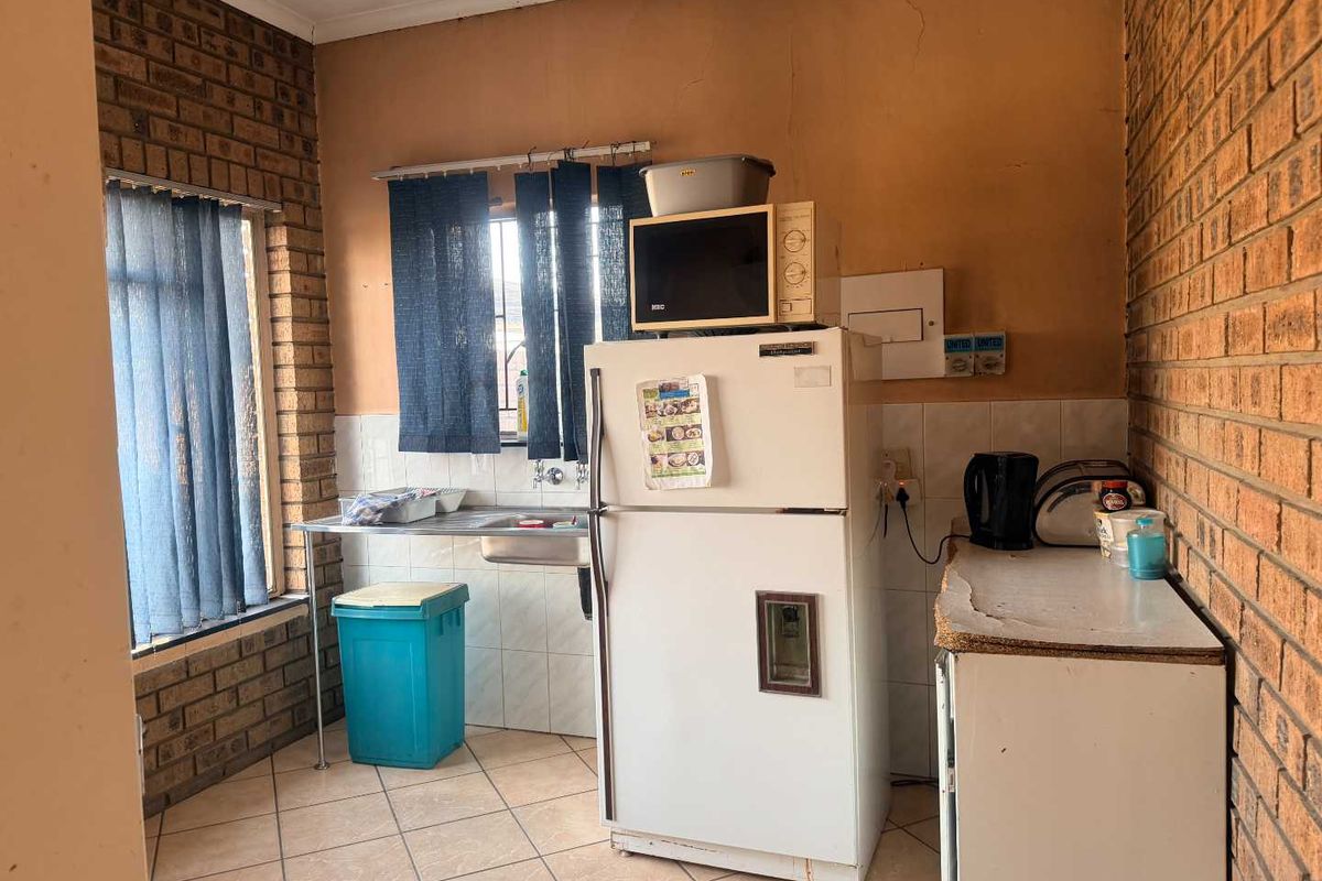 A functional kitchen area featuring exposed brick walls, tiled flooring, and a stainless steel sink with tiled splashback.