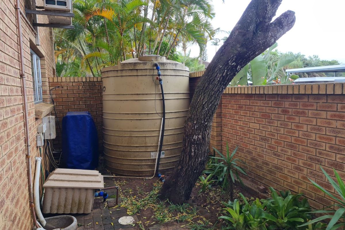 Exterior side area featuring a large water storage tank, brick boundary wall, and established garden vegetation.