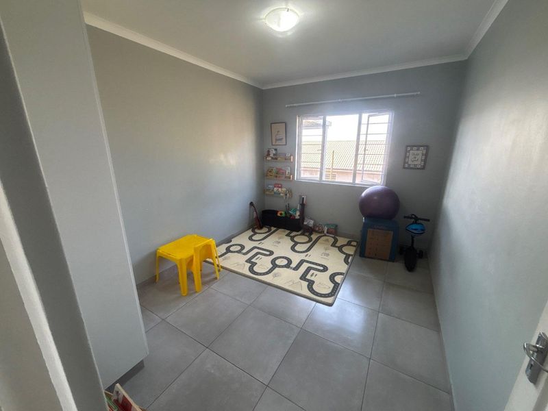 A functional bedroom featuring neutral grey walls, large format floor tiles, and a window providing natural light.