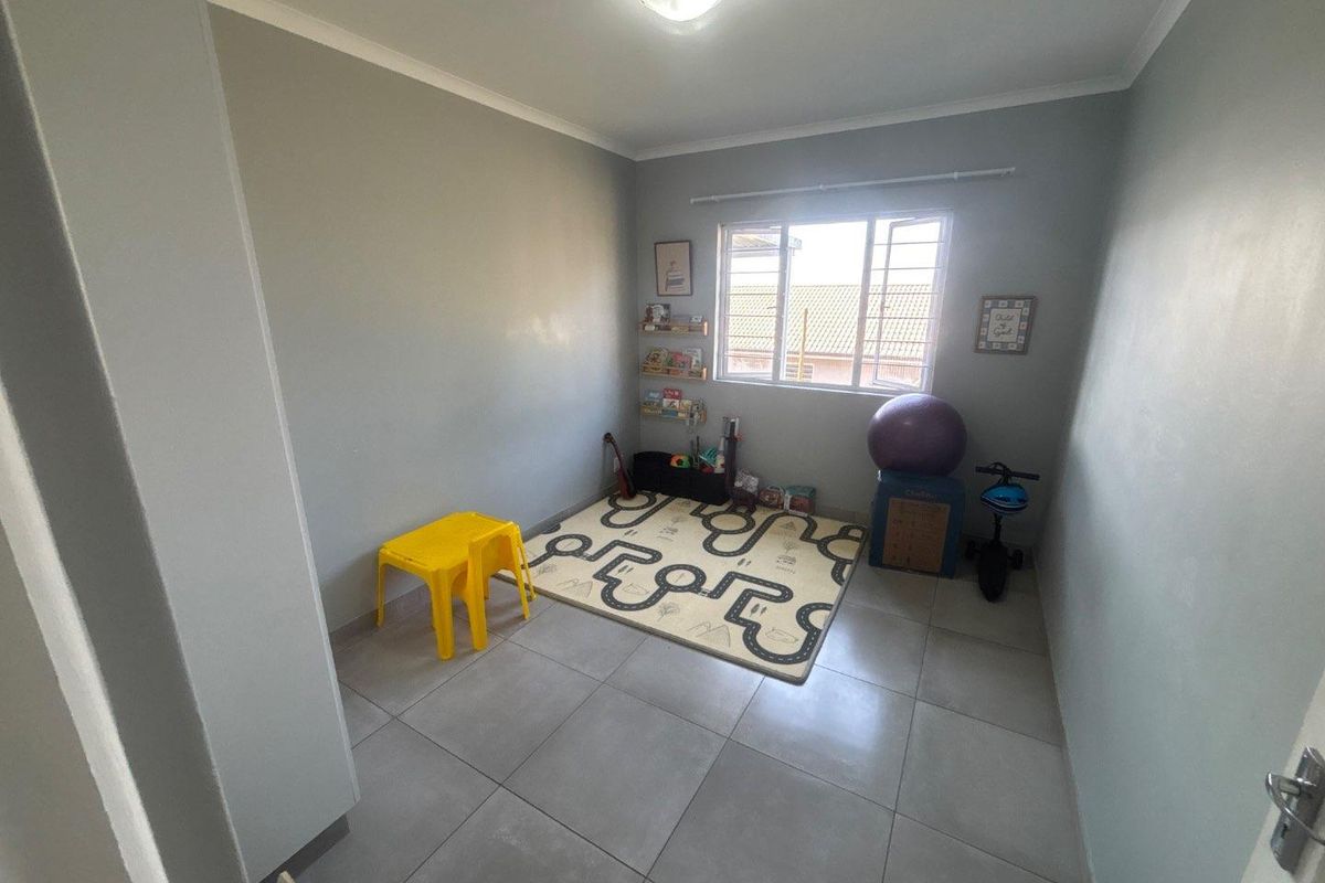 A functional bedroom featuring neutral grey walls, large format floor tiles, and a window providing natural light.