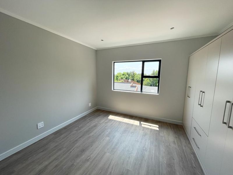 A bright, modern bedroom featuring neutral walls, durable laminate flooring, and ample built-in cupboard storage with a pleasant exterior view.