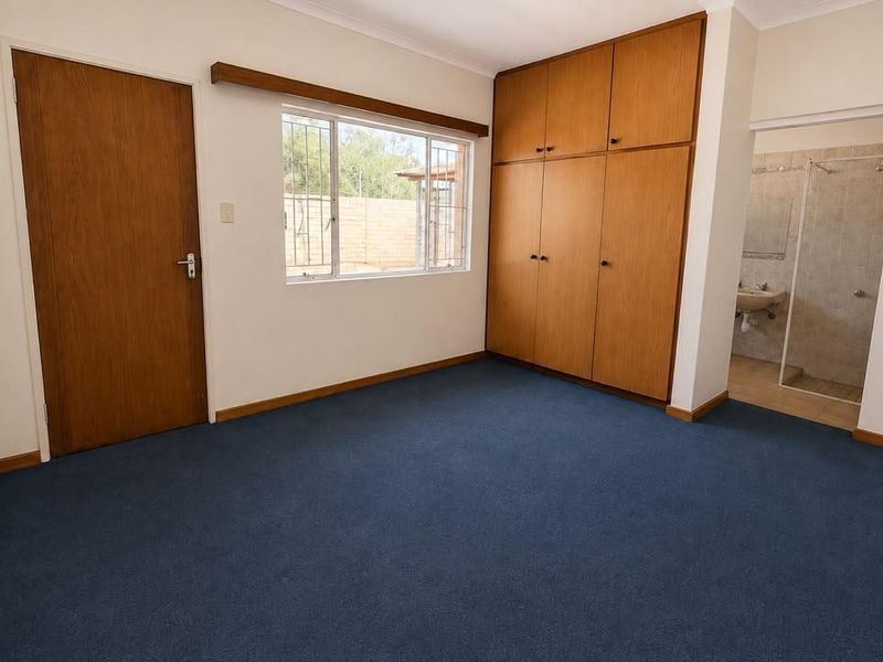 A spacious bedroom featuring built-in wooden cupboards, blue carpeting, and direct access to an en-suite bathroom.