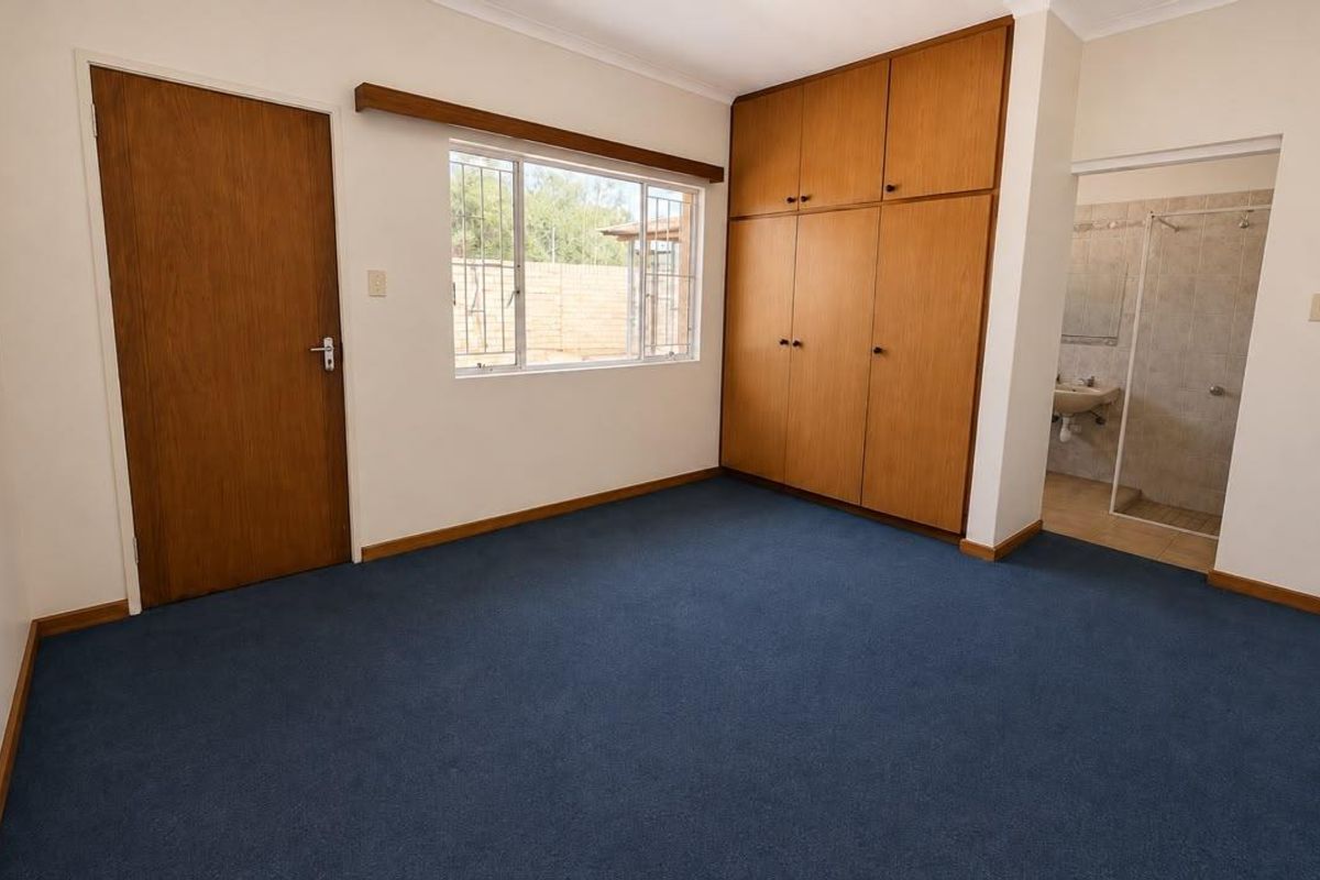 A spacious bedroom featuring built-in wooden cupboards, blue carpeting, and direct access to an en-suite bathroom.