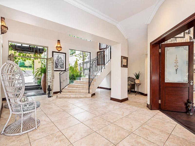 Spacious entrance hall featuring tiled flooring, a grand staircase with wrought iron railing, and a decorative timber front door leading to an outdoor area.