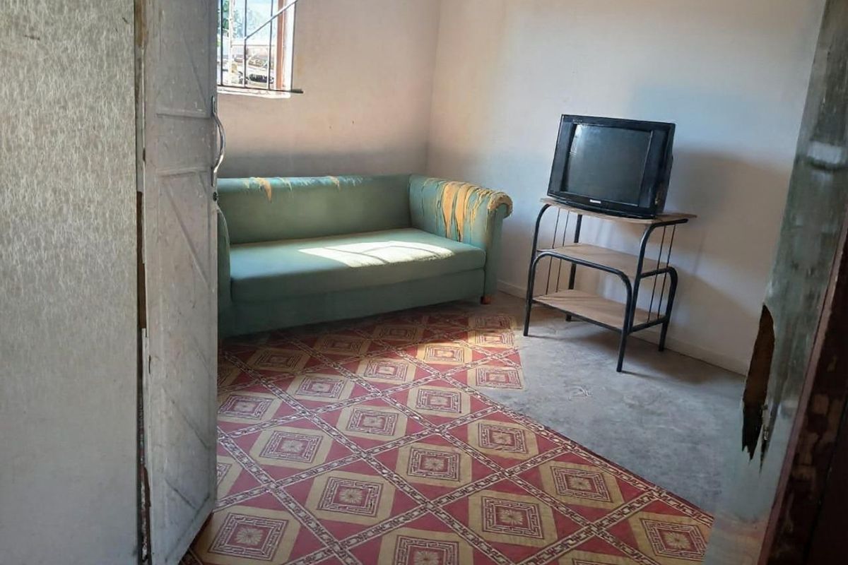 A small living area featuring patterned vinyl flooring and a window with security bars, requiring cosmetic updates to improve its overall condition.