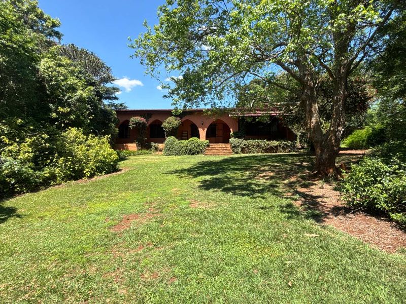 A view of the rear of the house featuring a classic arched veranda and a spacious, well-established garden with mature trees.