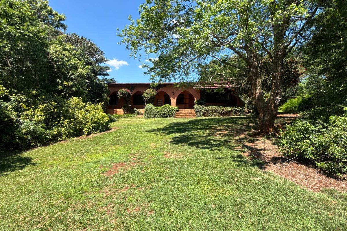 A view of the rear of the house featuring a classic arched veranda and a spacious, well-established garden with mature trees.