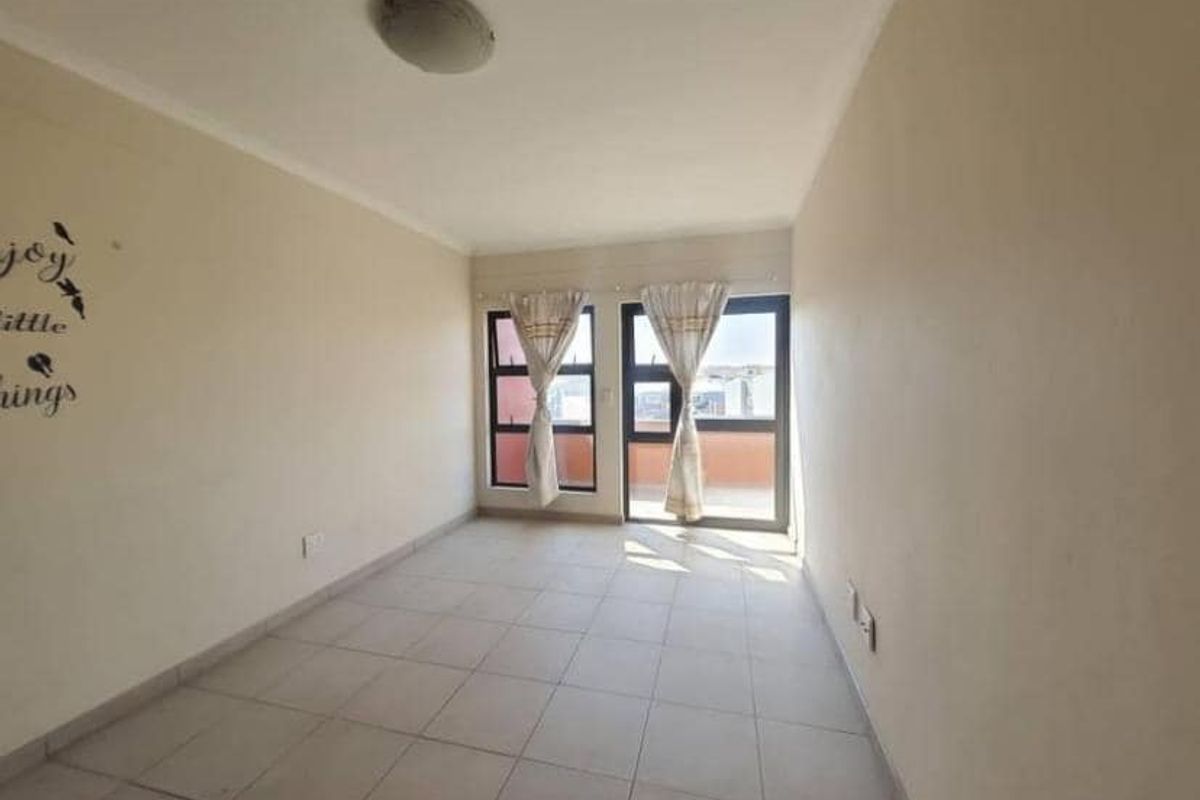 A bright, empty living area featuring neutral tiled flooring and large windows that provide natural light and access to the balcony.