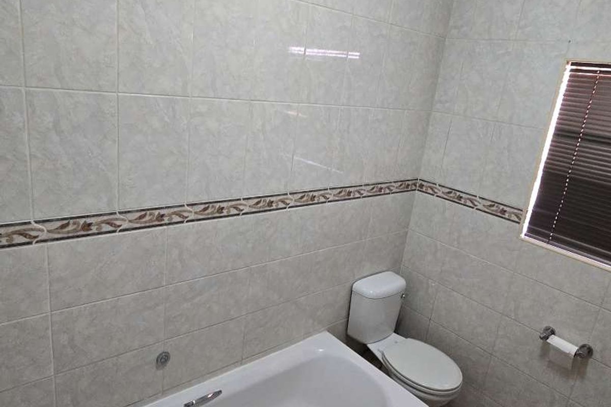 A functional bathroom featuring a standard bathtub, toilet, and full-height wall tiling with a decorative border.