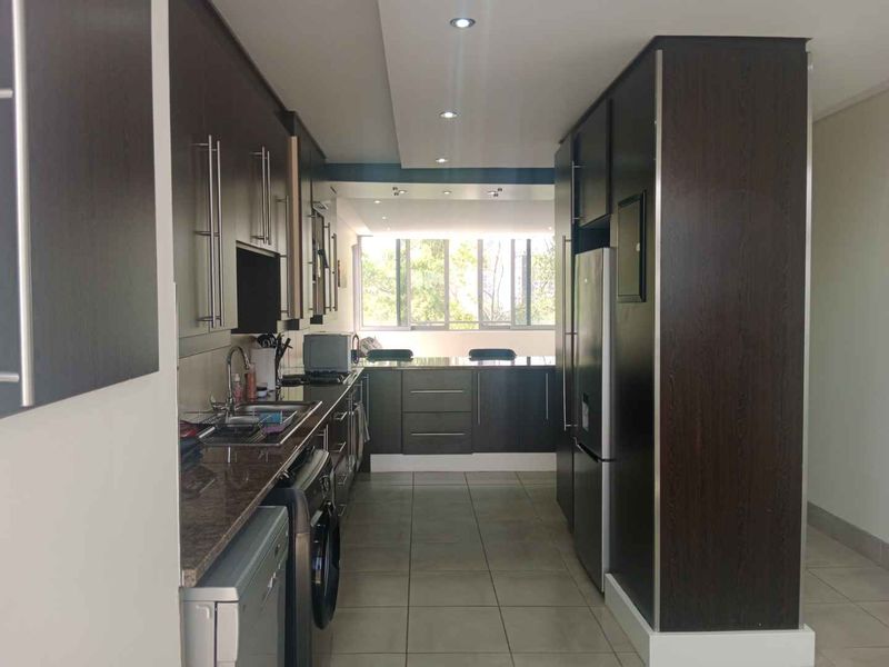A functional galley-style kitchen featuring dark wood cabinetry, granite countertops, tiled flooring, and recessed lighting, offering a clean and modern aesthetic.