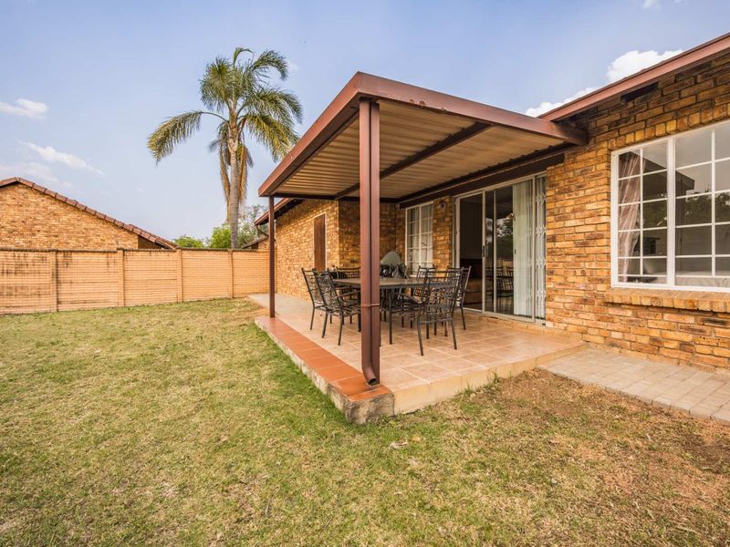 A covered brick patio area featuring tiled flooring and sliding glass door access, overlooking a private garden with a boundary wall.