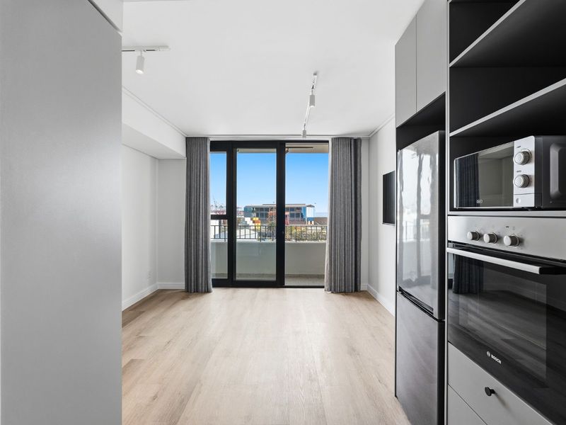 Modern open-plan living area featuring light laminate flooring, built-in kitchen appliances, and direct access to a private balcony with urban views.
