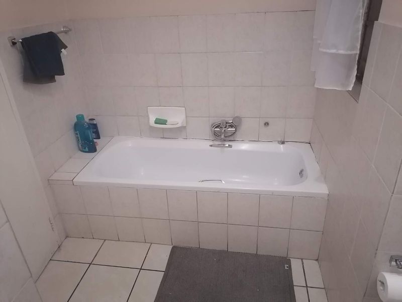 A functional bathroom featuring a built-in bathtub with white ceramic wall and floor tiling.