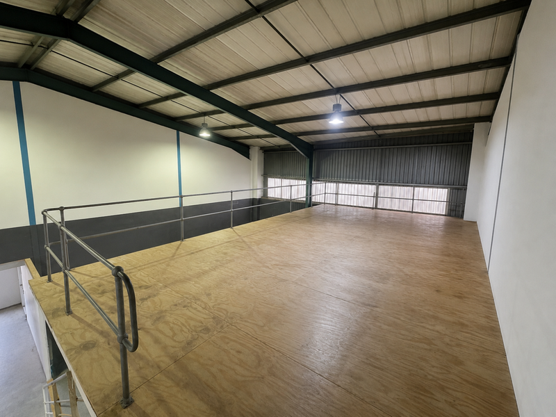 A clean, open-plan mezzanine level featuring industrial steel beams, plywood flooring, and safety railings, suitable for storage or additional workspace.