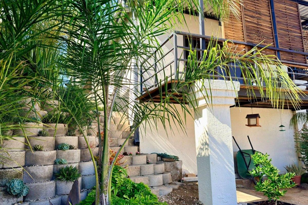 A multi-level outdoor area featuring a terraced retaining wall, a raised wooden deck with metal railings, and a covered patio space below.