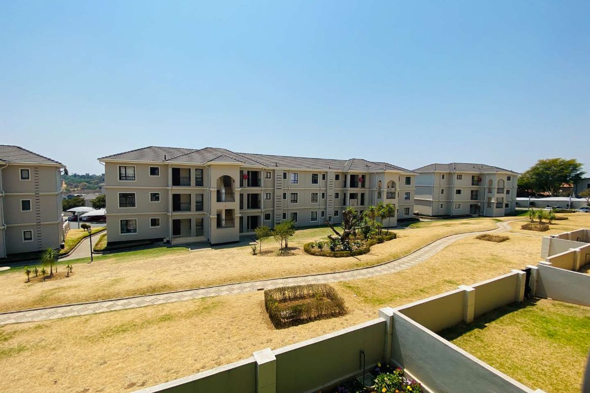 An elevated view of the apartment complex grounds, featuring multi-story residential buildings, paved walkways, and landscaped garden areas.