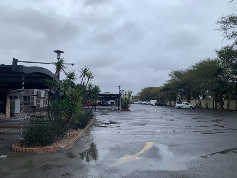 Industrial property exterior featuring an expansive asphalt parking area with covered bays and external air conditioning units.