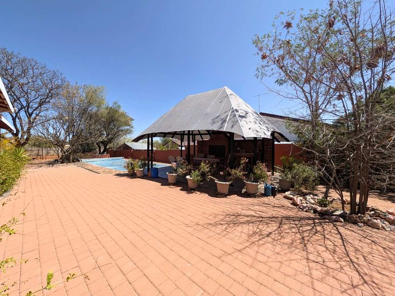 Outdoor entertainment area featuring a swimming pool and a covered thatched lapa with a built-in braai, set within a paved garden space.