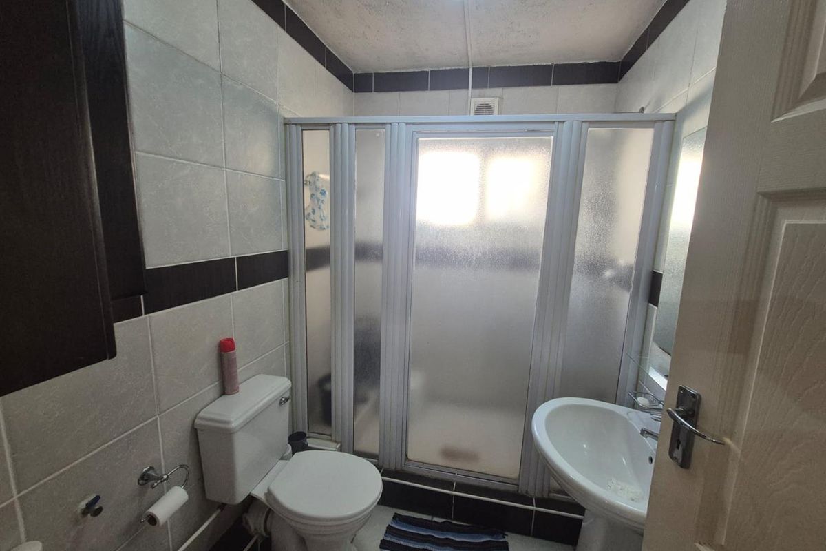 A compact bathroom featuring a shower enclosure, pedestal basin, and toilet with dated wall tiling and visible ceiling wear.