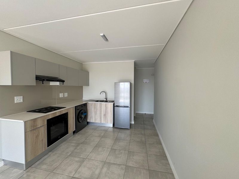 Modern kitchen featuring sleek cabinetry, stone countertops, built-in oven, hob, extractor fan, and tiled flooring in an open-plan layout.
