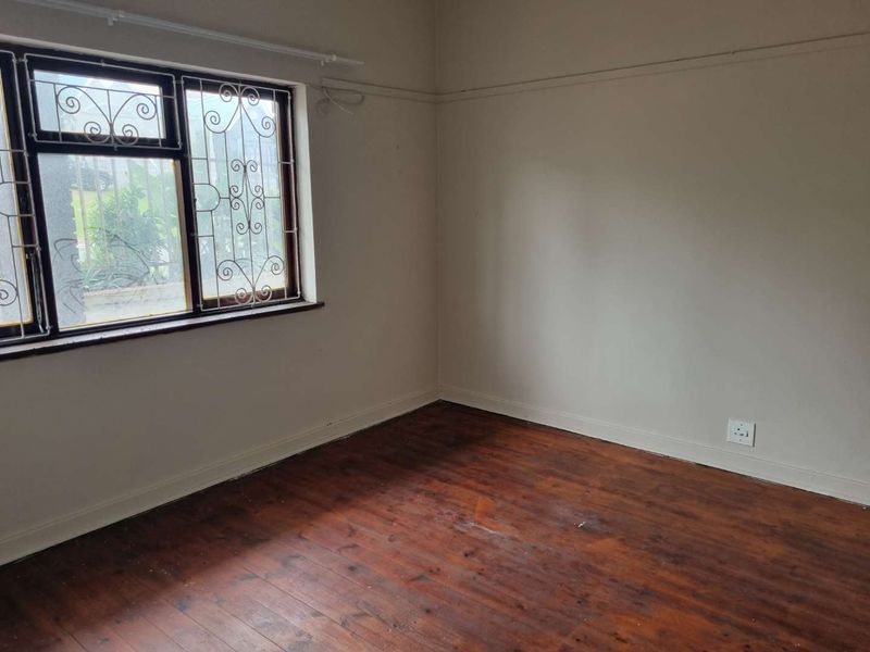 An empty bedroom featuring original timber flooring, a picture rail, and security bars on the window.