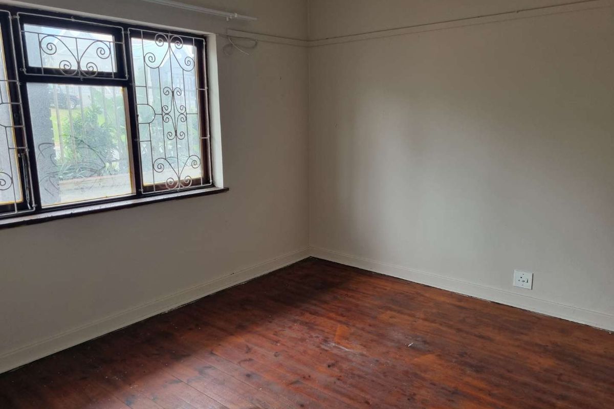 An empty bedroom featuring original timber flooring, a picture rail, and security bars on the window.