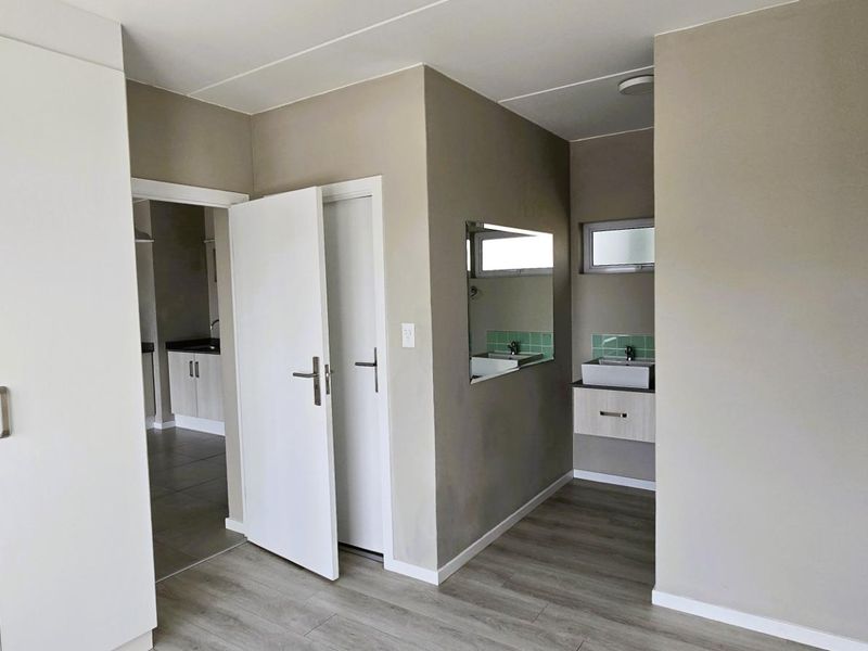 A clean bedroom featuring built-in wardrobes, laminate flooring, and an integrated vanity area with a basin and tiled splashback.