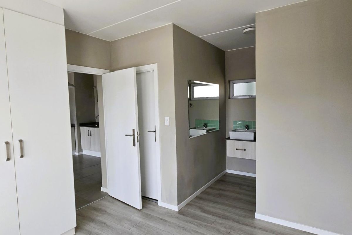 A clean bedroom featuring built-in wardrobes, laminate flooring, and an integrated vanity area with a basin and tiled splashback.